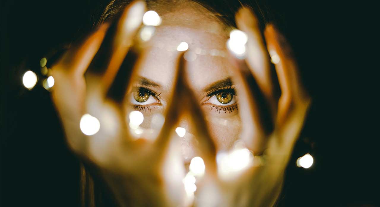 Mulher a ver através das suas mãos com luzes representando a descoberta de novas tendências